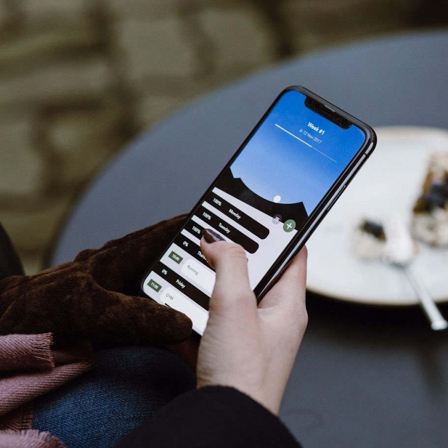 Person hält ein Smartphone mit einer App-Anzeige und einem blauem Himmel im Hintergrund.